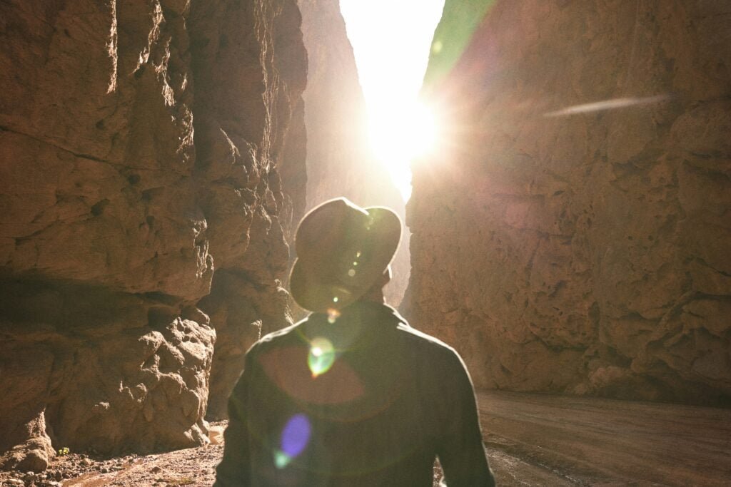 a man standing in a canyon with the sun shining through the rocks